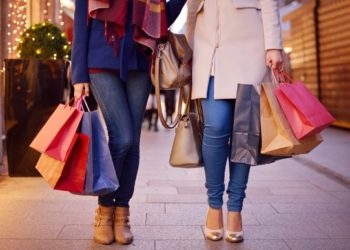 Young women shopping in the city, legs and hands close up, carrying paper bags.