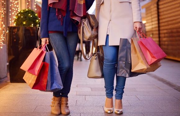Young women shopping in the city, legs and hands close up, carrying paper bags.